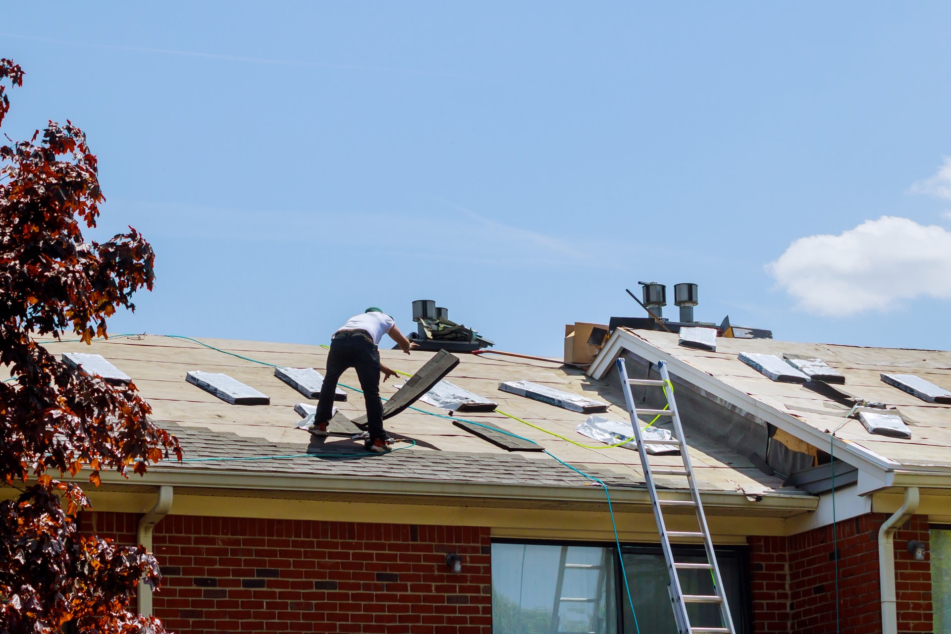 Roofers placing shingles for roof repair on a roof with a ladder leaning against it.